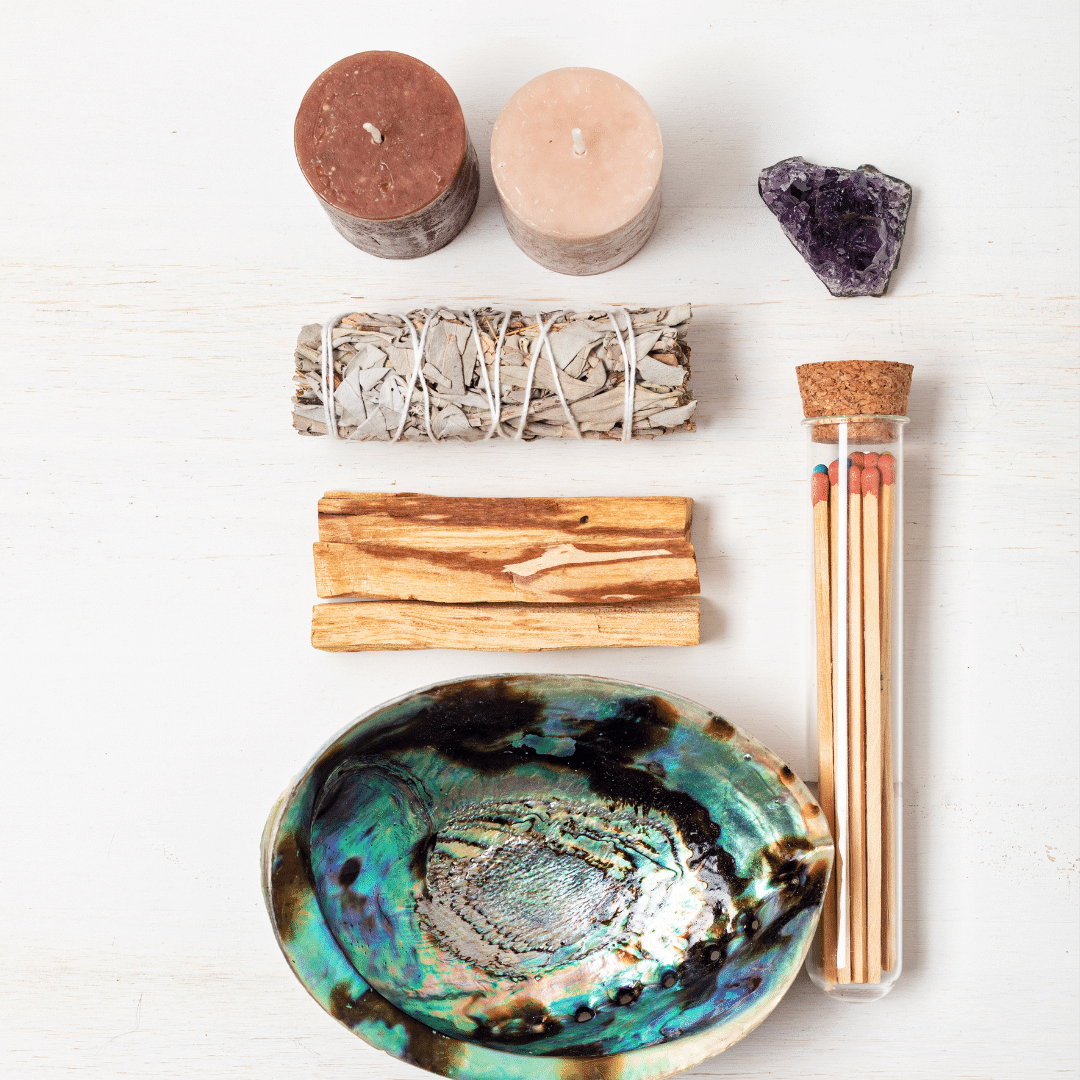 A picture of an abalone shell, mathces, palo santo, sage, an amethyst crystal and 2 candles.